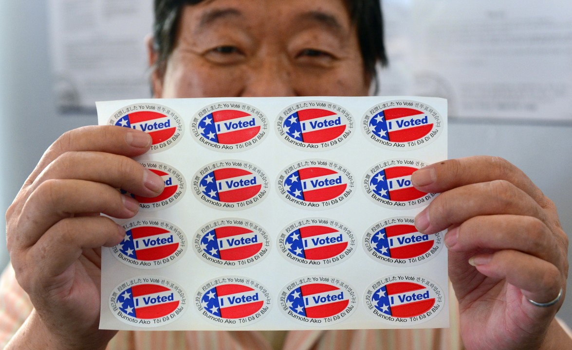 A person holds a sheet of multilingual “I Voted” stickers.